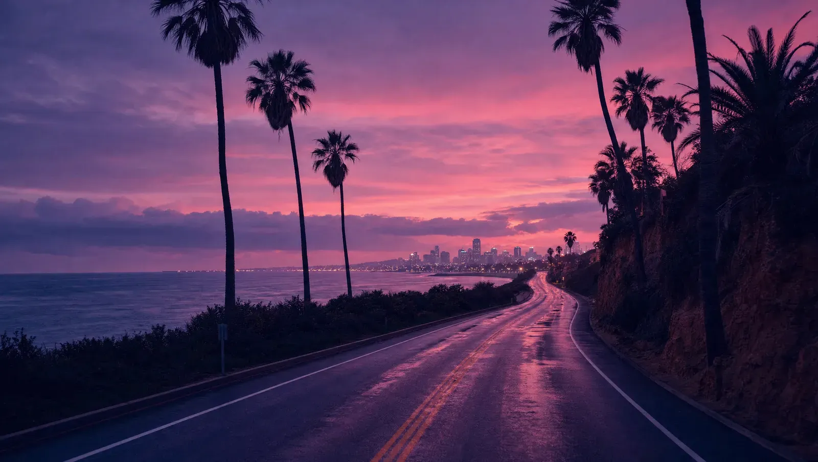 An empty coastal highway lined with palms at blue hour, a city glowing on the horizon