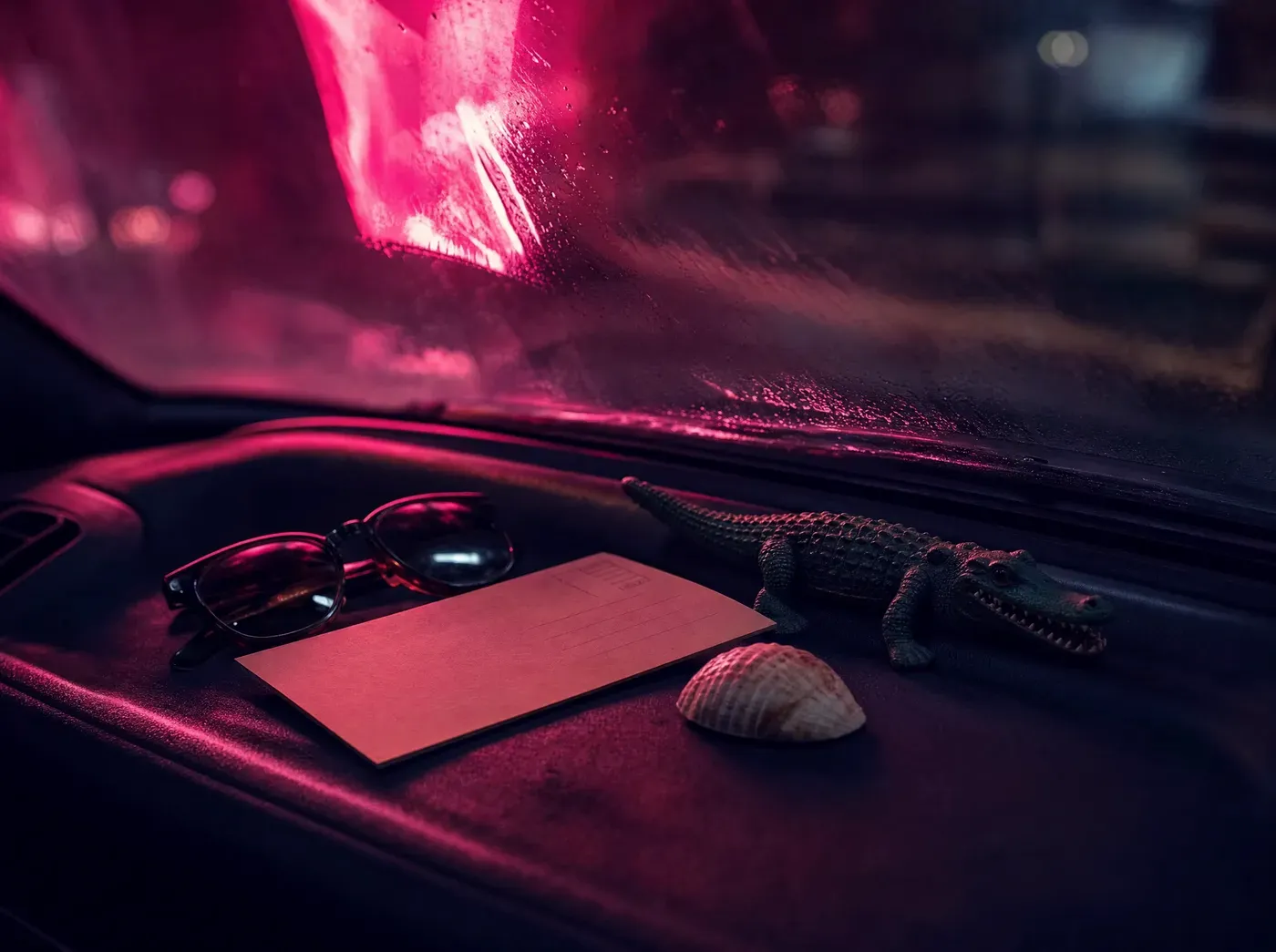 A seashell, sunglasses and keepsakes on a car dashboard under neon light