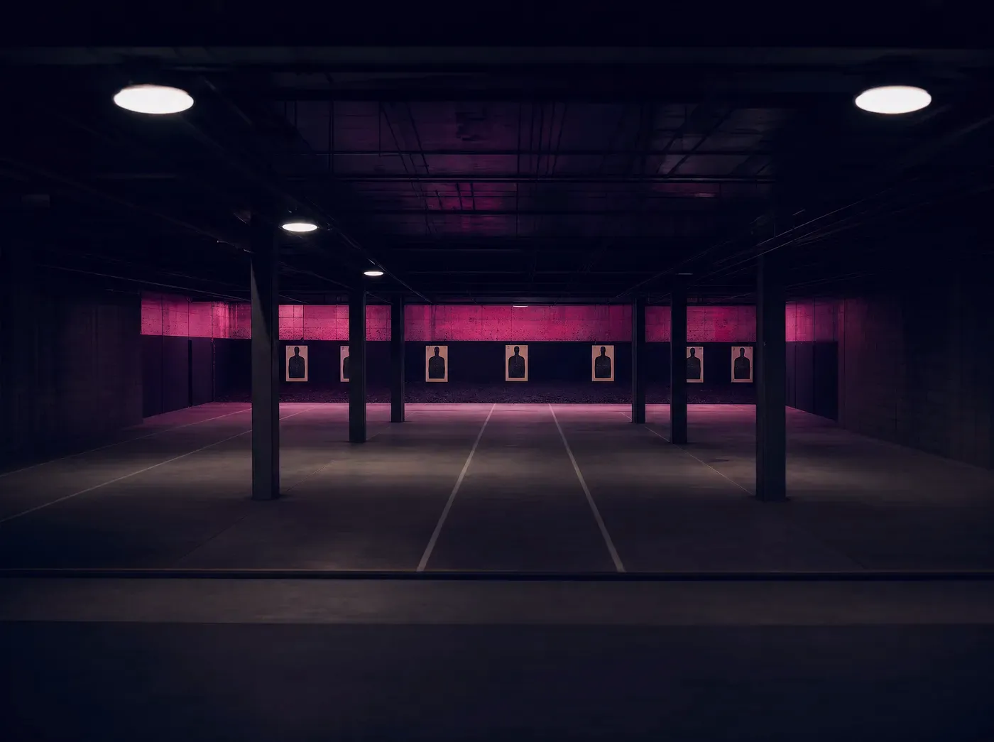 An empty practice range with paper targets under overhead lamps